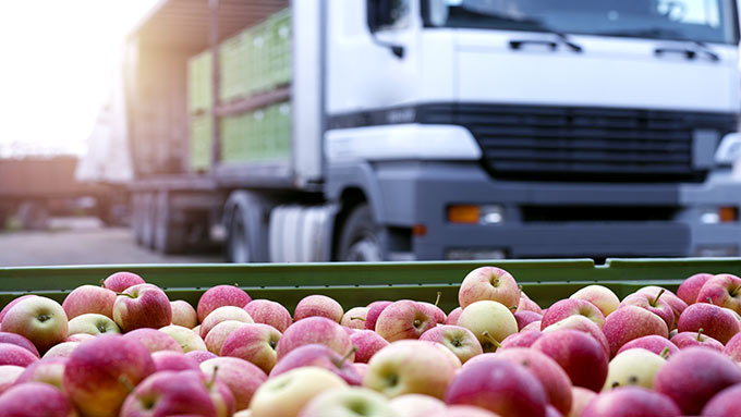 Uma bandeja de maçãs em primeiro plano com um caminhão branco de entrega de alimentos ao fundo